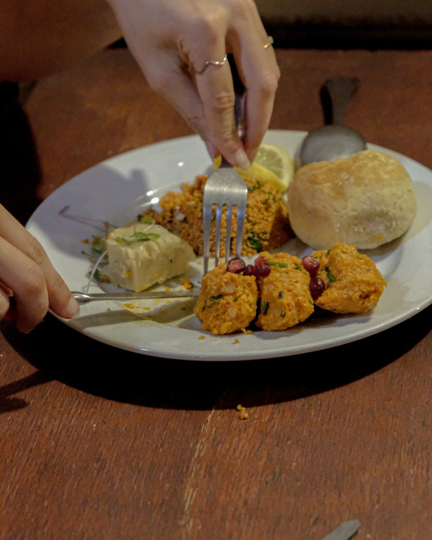 A guest digging into a vegan meze plate: çiğ köfte with pomegranate, kısır, hummus, lemon and fresh bread