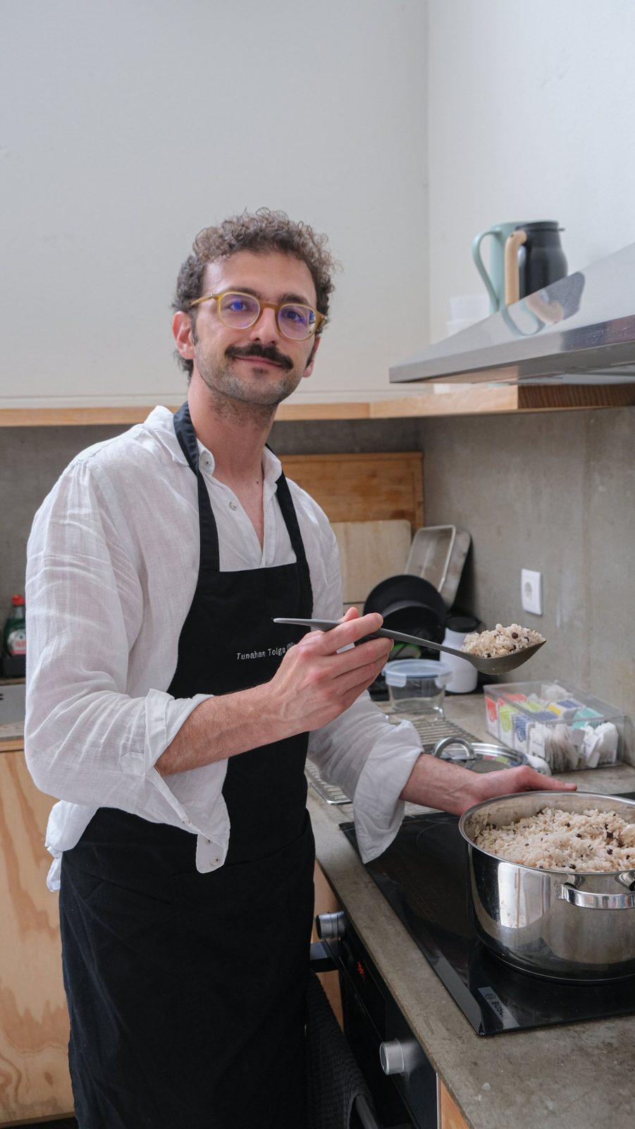 Tuna in his apron at the stove, holding a spoon of pilav